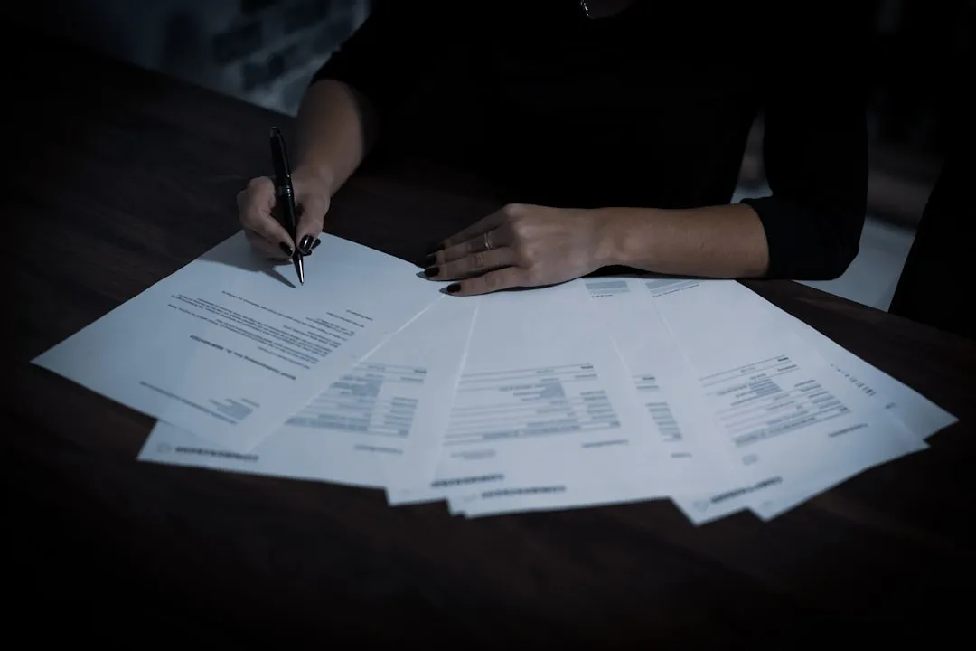A person organizing documents in a folder with a stamp, with a printer in the background, in an administrative setting.